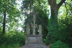 Oberhalb des Friedhofs Oberpleis Steindenkmal zu Jesus am Kreuz, in der Mitte angeordnet, daneben Mutter Maria auf der linken Seite, auf der anderen eine Figur, der der Kopf fehlt.